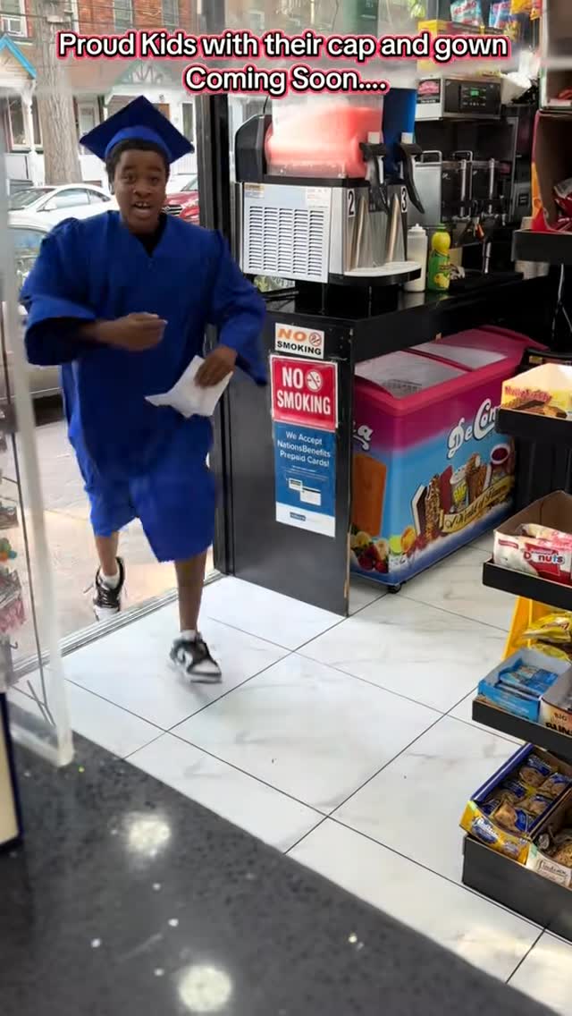 A student in a blue graduation cap and gown entering a neighborhood deli.