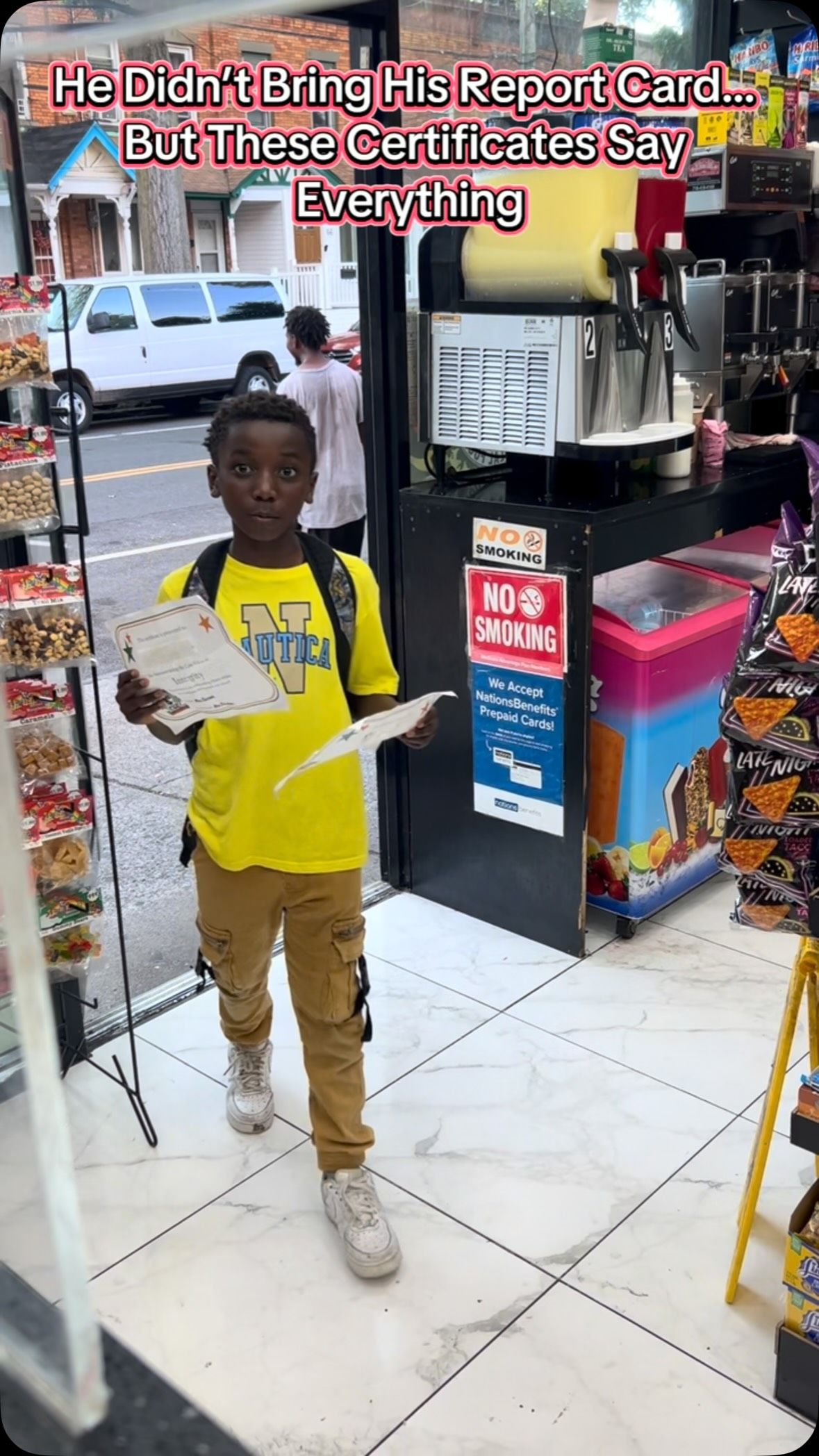 A student holding two achievement certificates inside a neighborhood deli.